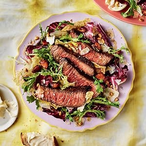 pink plate holding lettuces and sliced steak salad on a yellow tie dye tablecloth