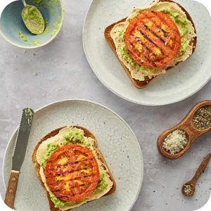 2 plates with slice of whole grain toast with chickpea paste, avocado, grilled tomato.