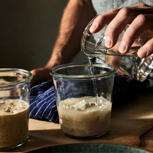 author pouring water into a glass with sourdough starter