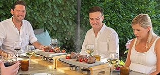 friend eating round a table with their hot stone cooking sets cooking steak on a stone