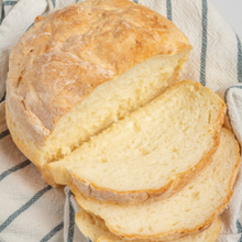 A round loaf of bread, partially sliced. The bread is soft and bendable.