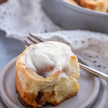 a single cinnamon roll on a gray plate with lace napkin and fork in the background