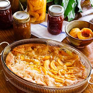 A thin metal oval serving dish filled with sliced peaches. Four jars of sliced peaches in back.