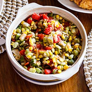 A round serving dish filled with succotash (lima beans, corn, and tomatoes).