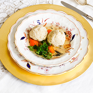 Two matzo balls in a decorative bowl sitting in medium and large plates.