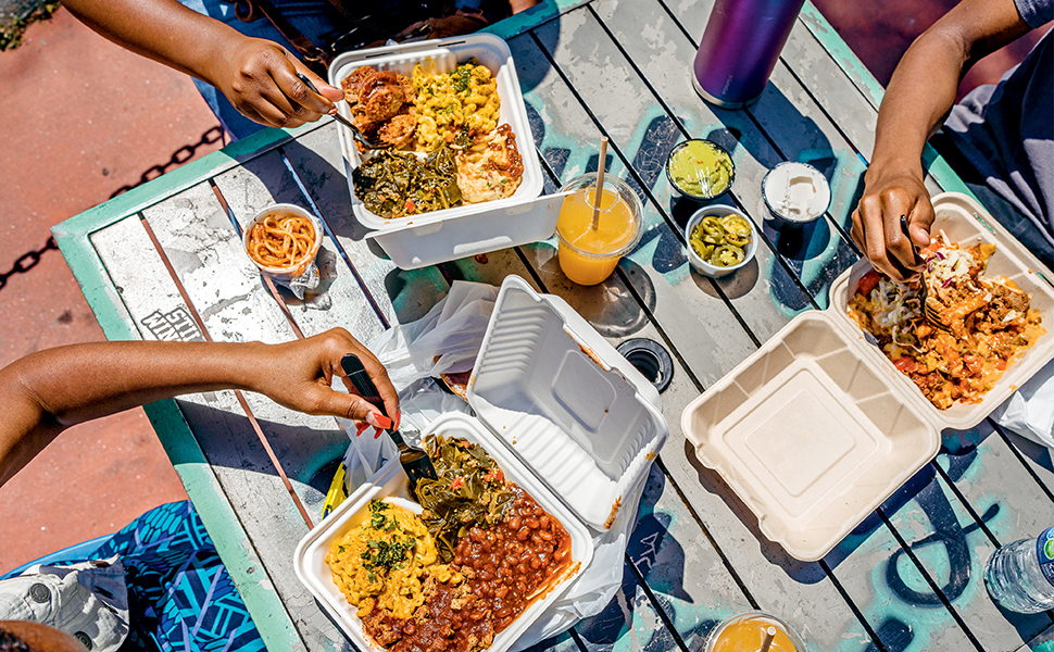 overhead shot of people eating barbecue food in takeout containers outside at picnic table