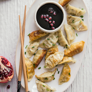 A photo of Simanim Potstickers with Pomegranate Dipping Sauce on a plate with chop sticks. 