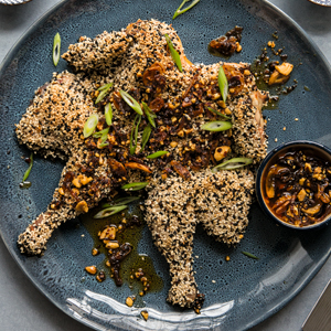 A photo of Spatchcock Sesame Chicken on a blue with dipping sauce 