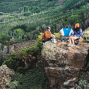 Two people sitting having lunch on the top of a cliff. 